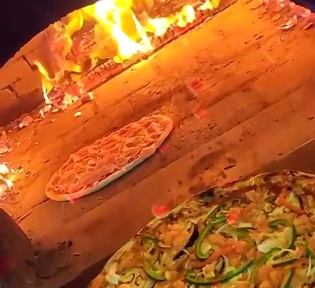 Interior del horno de leña de Mambo Italiano con el fuego encendido y dos pizzas horneándose